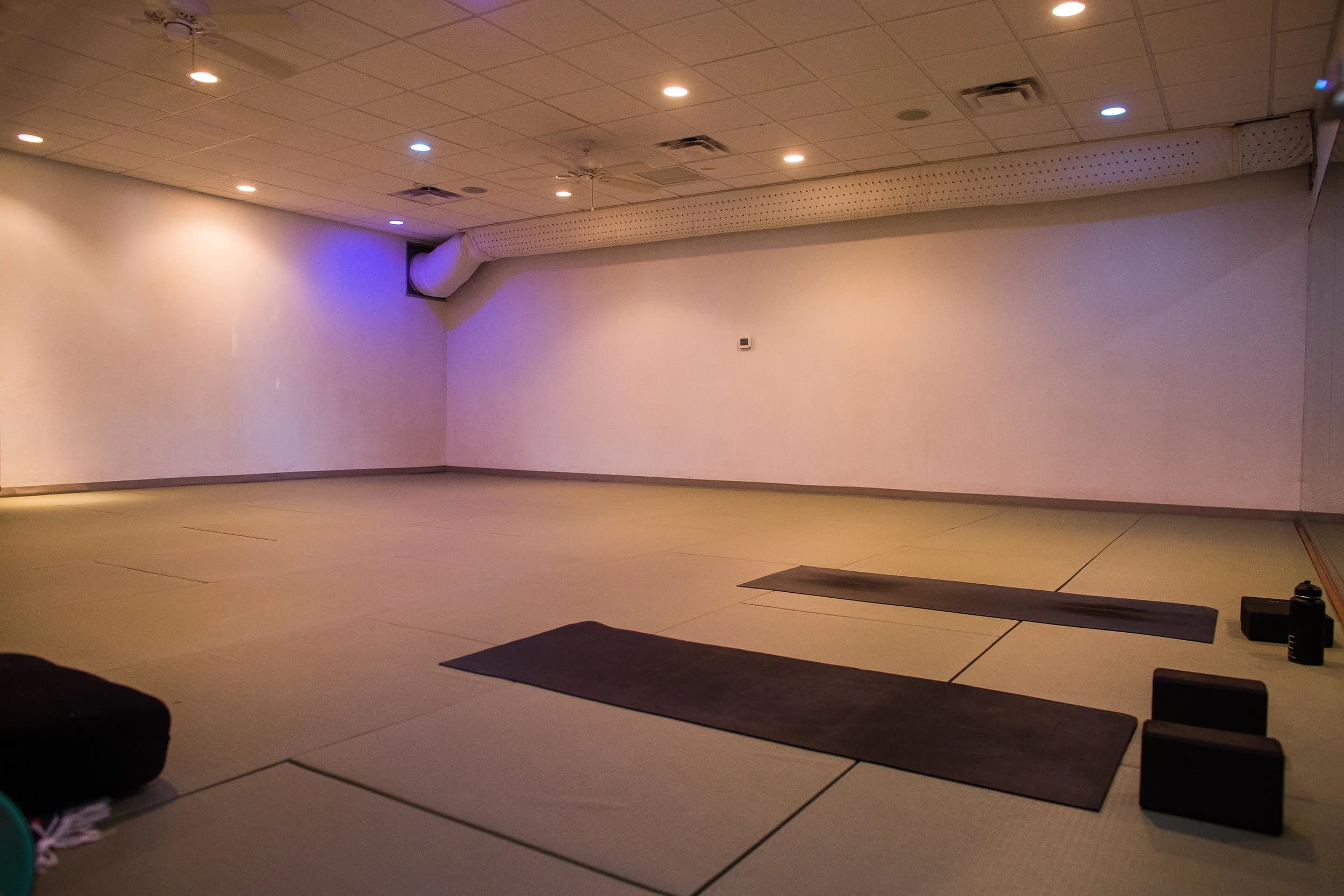 Studio A rental space with padded flooring, warm lighting, and yoga mats laid out